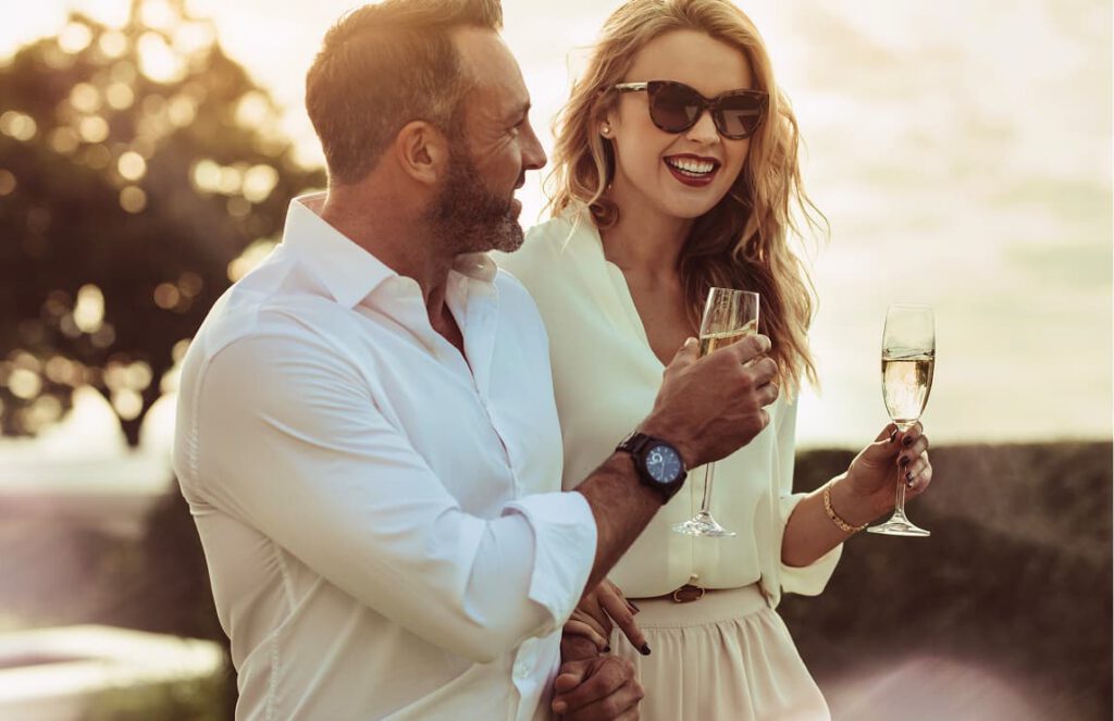 Man and woman dressed in white on vacation enjoying champagne at sunset